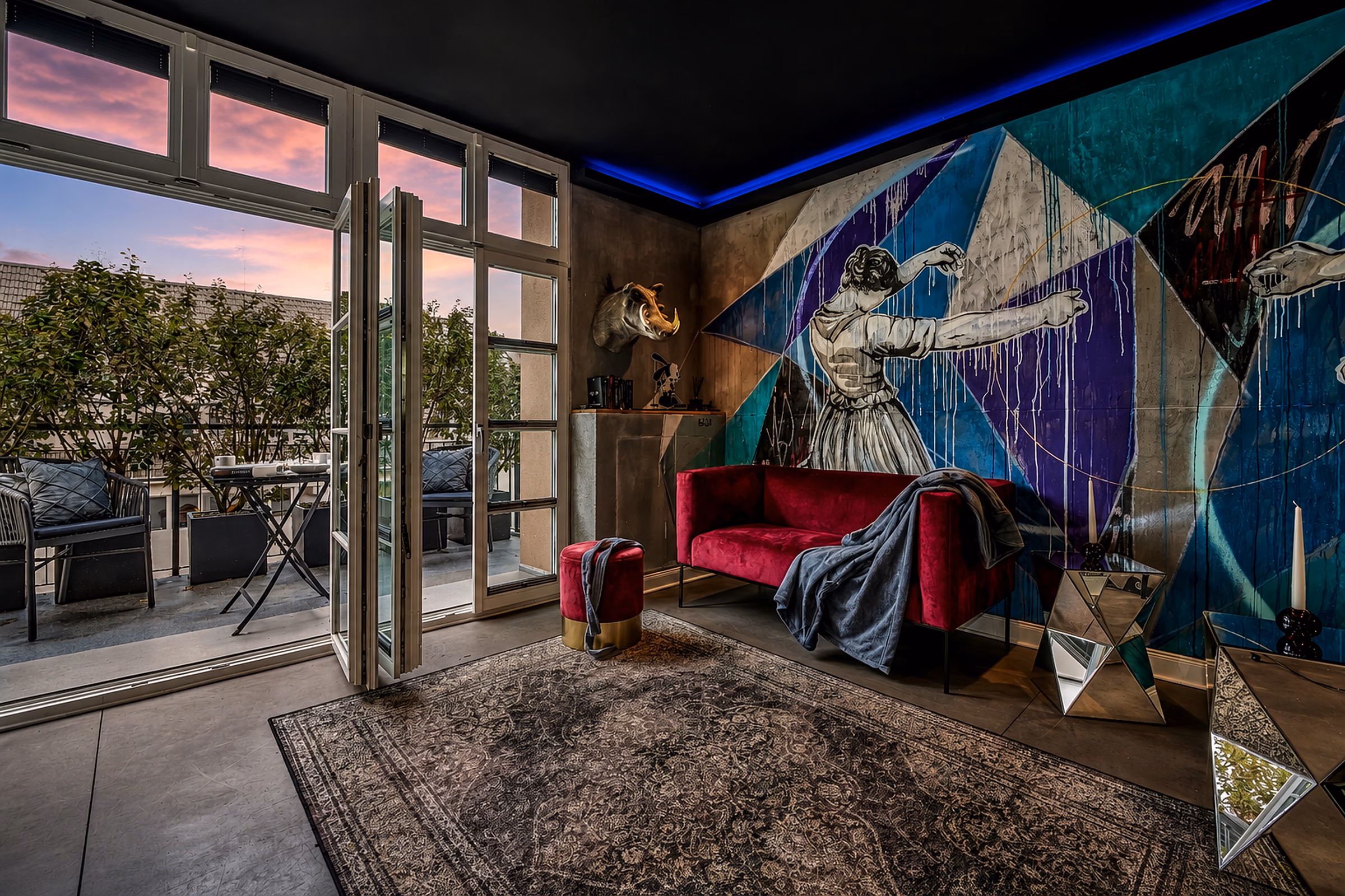 Living area in the Executive Design Loft Heidelberg with statement mural, red sofa and direct balcony access