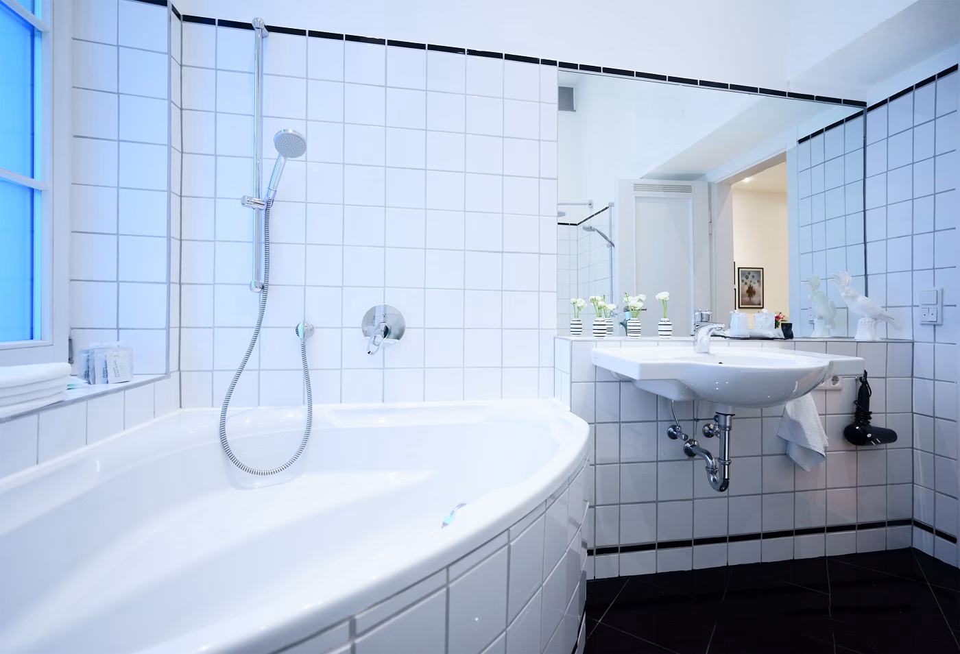 Modern bathroom with white tiled walls, bathtub with shower, and sink with large mirror at Boutique Suites and Residences Heidelberg.