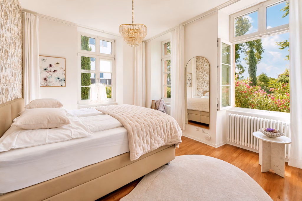 Bright bedroom in the Imperial Suite Heidelberg with large windows, floral wallpaper, and a view of the garden – ideal for long-term stays.