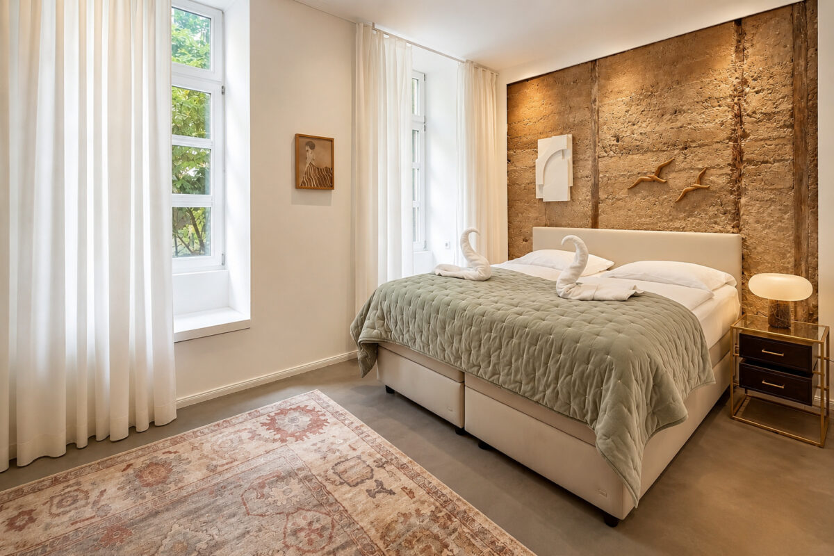 Private king bedroom with natural stone feature wall in the Business One-Bedroom Residence Heidelberg