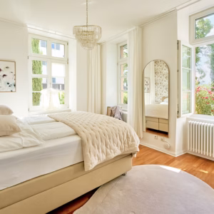 Bright bedroom in the Imperial Suite Heidelberg with large windows, floral wallpaper, and a view of the garden – ideal for long-term stays.