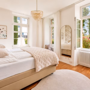 Bright bedroom in the Imperial Suite Heidelberg with large windows, floral wallpaper, and a view of the garden – ideal for long-term stays.