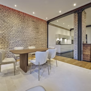 Spacious dining area with designer chairs, exposed brick walls, and direct connection to the modern kitchen – refined living in the Grand Residence Heidelberg.