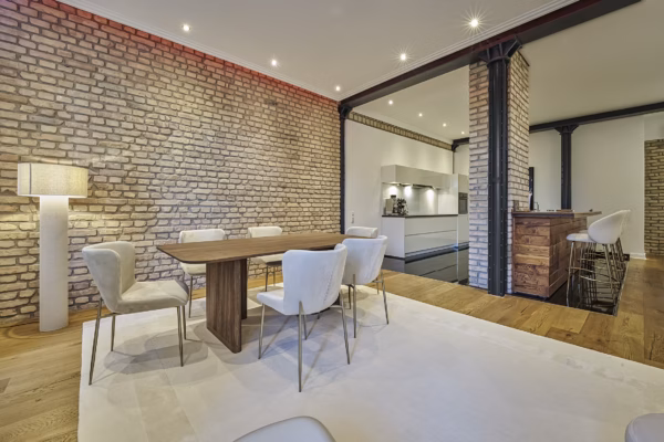 Spacious dining area with designer chairs, exposed brick walls, and direct connection to the modern kitchen – refined living in the Grand Residence Heidelberg.