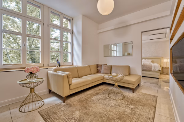Bright living area with large windows, leather sofa, and stylish décor in the Grand Superior Suite Heidelberg – designed for long-term luxury stays.