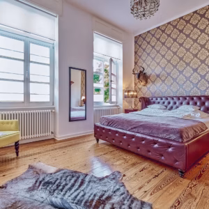 Spacious boutique apartment bedroom with vintage leather bed, chandelier, and classic wallpaper – ideal for long-term stays in Heidelberg